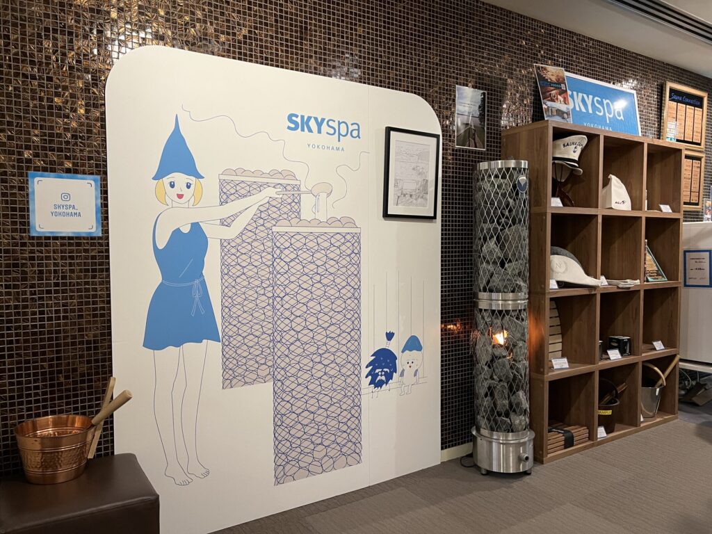 スカイスパYOKOHAMA サウナ室前 ロウリュ説明とサウナハット棚